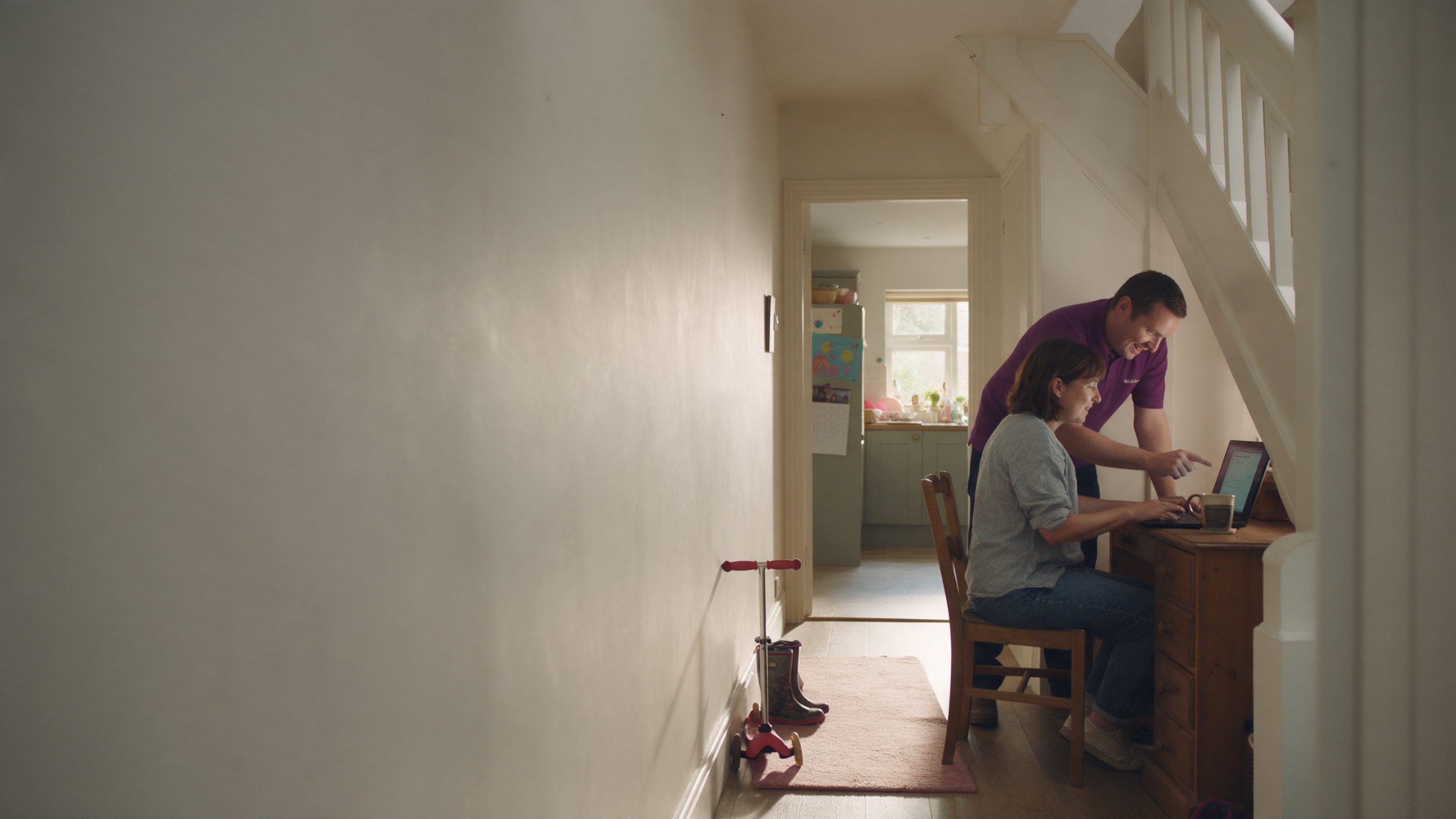 An Ashburn Stone technician leaning over a customer sat at a desk in her hallway, pointing something out on her laptop screen